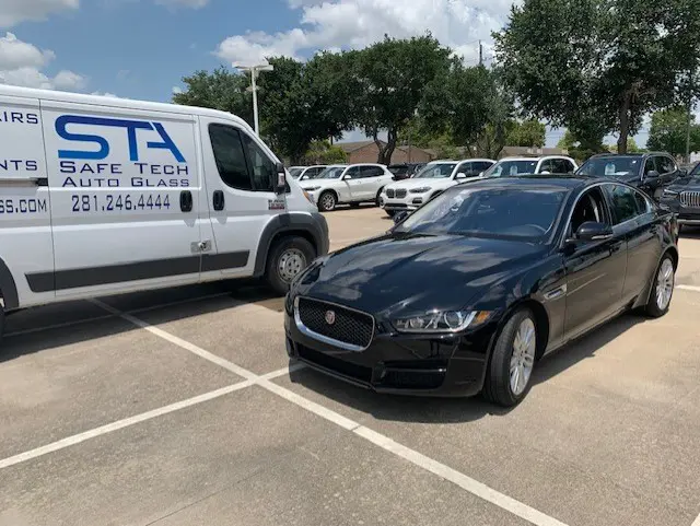 A black car parked in the parking lot next to a white van.