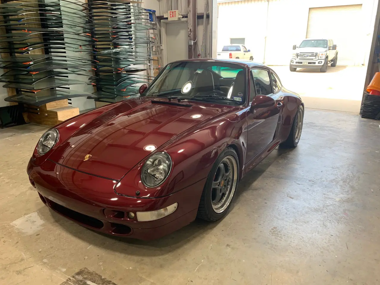 A red car parked in a garage next to stacks of other cars.